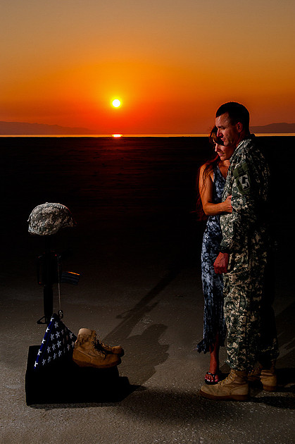 Soldier looks down on field cross with his wife by his side