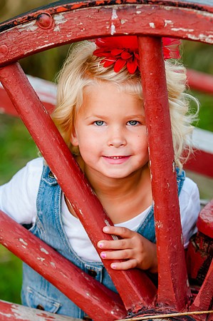 Girl poses behind red wagon wheel for family pictures