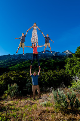 A family of five, with the father balancing the mother and three children on his hands above his head, forming an arrow shape.