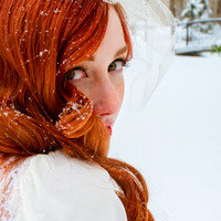 Vintage bride with snowflakes in her gorgeous red hair with snow covered bridge in background.