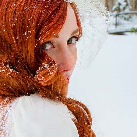 Vintage bride with snowflakes in her gorgeous red hair with snow covered bridge in background.