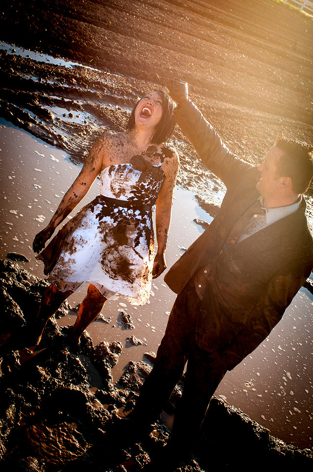 Groom squishes handful of mud on bride's head
