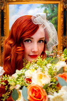 Beautiful vintage red haired bride with a floral bouquet from Studio Stems in the foreground and a painting at the Woods on Ninth in the background.