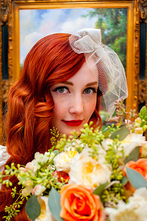 Beautiful vintage red haired bride with a floral bouquet from Studio Stems in the foreground and a painting at the Woods on Ninth in the background.