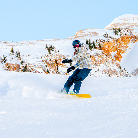 Snowboarder leaving a powder trail on a bluebird day with a mountain background at Snowbird