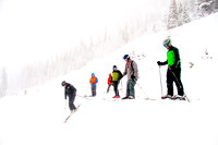 Picture of skiers dropping in to a steep bowl with low visibility.