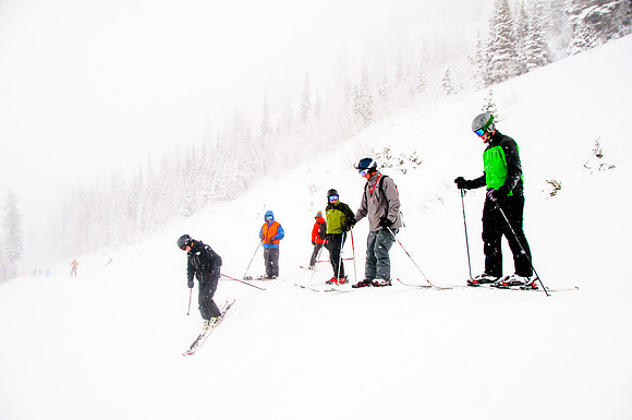 Picture of skiers dropping in to a steep bowl with low visibility.