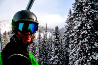 Portrait of a skier on a lift with snow covered trees and blue skies