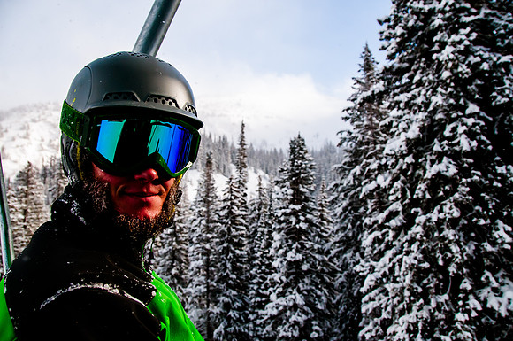 Portrait of a skier on a lift with snow covered trees and blue skies
