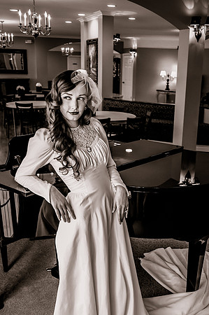 Black and white 40's vintage bride leaning against piano with wedding dress wrapped around piano leg