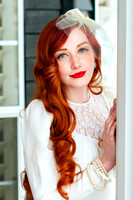 Bride with red hair poses in front of a cool colored background