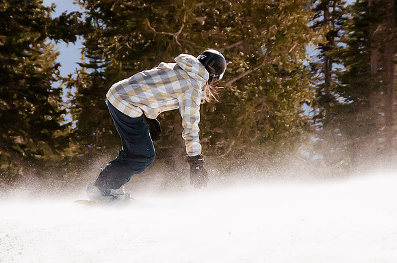 Snowboarder reaching down into the wind blown snow